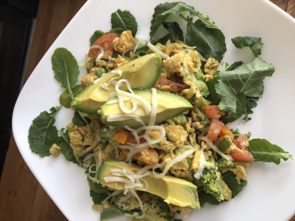 Healthy veggie omelette in a bed of kale topped with avocado.